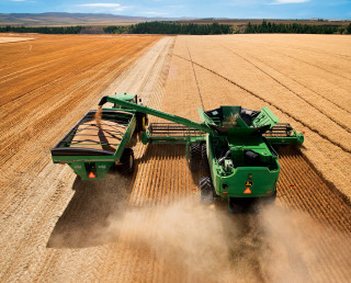 Green tractor driving field grain - a machine free wallpaper