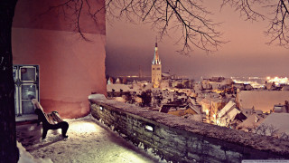 Person sitting ledged snow city - a clock tower in the distance free wallpaper