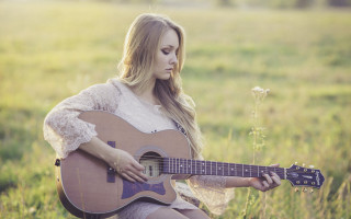 Woman sitting field playing guitar - a guitar free wallpaper