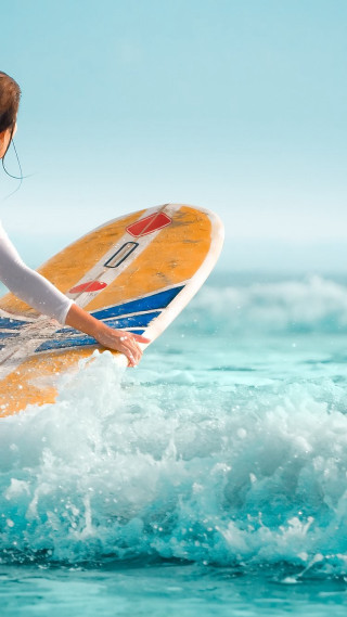 Woman holding surfboard riding wave - sunny free wallpaper for mobile