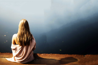 Woman sitting ledge water mountains - liminal space free wallpaper