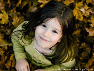 Little girl smiling leaves ground 2 - free portrait wallpaper for desktop