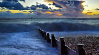 Beach waves fence sunset clouds - a light house in the distance free wallpaper