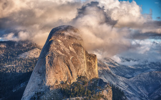 Tall mountain rock face clouds - a forest below free wallpaper