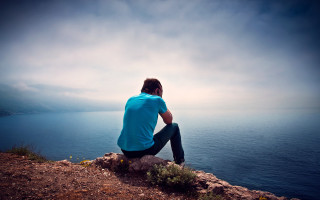 Man sitting rock ocean cloudy - liminal space free wallpaper for desktop