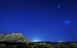 Mountain blue sky stars trees - a bright light in the distance free wallpaper
