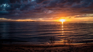 Sunset water clouds beach footprints - a sunset over a body of water free wallpaper
