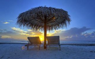 Beach sunset chairs umbrella ocean - the sun setting behind them free wallpaper