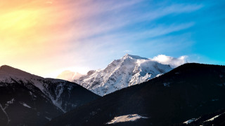 Mountain range snow covered summit - a bright sun in the sky above free wallpaper