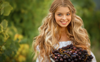 Woman grinning holding grapes outdoors - a green background behind her free wallpaper