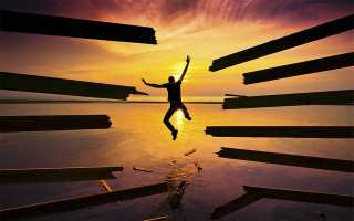 Man jumping over water sunset - his hands in free wallpaper