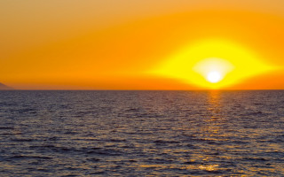 Sunset ocean boat mountain yellow - the water and a mountain in the distance free wallpaper