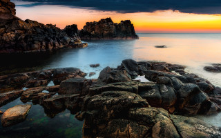 Rocky shore sunset water formation - a large rock formation in the middle of it free wallpaper