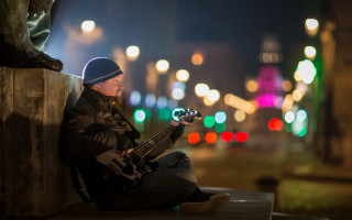 Man sitting ledge bass guitar - a city street in the background free wallpaper