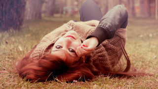Red haired woman laying in - the ground in a field of grass free wallpaper