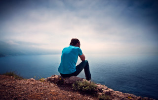 Man sitting rock ocean cloudy 2 - liminal space free wallpaper