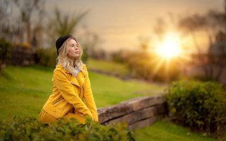 Woman yellow coat park sunset - the sun shining behind her free wallpaper
