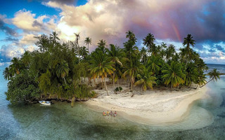 Small island palm trees boat - the water under a cloudy sky free wallpaper
