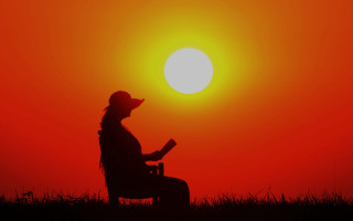 Woman sitting reading sunset silhouette - the sun setting behind her free wallpaper
