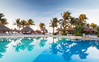 Thatched roof pool palm trees - a beach in the background free wallpaper