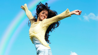 Cheerful woman jumping rainbow blue - a rainbow in the background free wallpaper