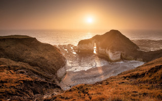 Sunset ocean rocky outcropping beach - a small boat free wallpaper for desktop