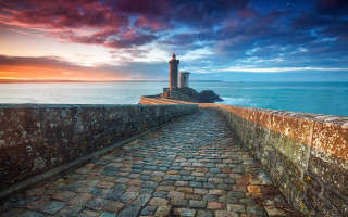 Stone lighthouse rocky shore sunset - a red sky in the background free wallpaper