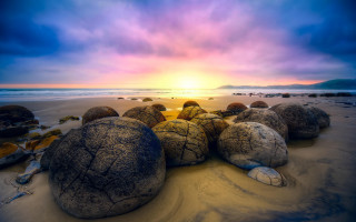 Rocks sandy beach cloudy sunset - the sun setting free wallpaper