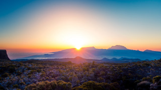 Sunset mountain range trees horizon 2 - a bright sun in the distance free wallpaper