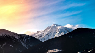 Mountain range snowy peak sunrise - a bright sun in the sky above free wallpaper