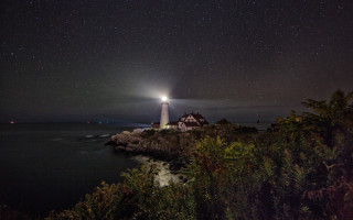Lighthouse rocky shore night stars 2 - a light house in the distance free wallpaper