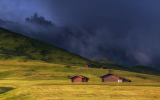 Grassy field two cabins dark - a mountain in the distance free wallpaper