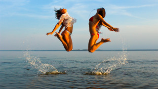 Two women jumping into water - a boat in the ocean free wallpaper