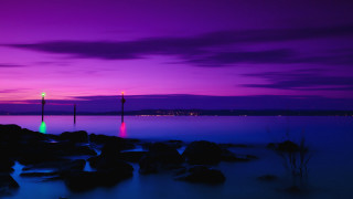 Purple blue sky lighttower rocks - the foreground and a body of water free wallpaper