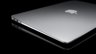 Silver apple laptop black surface - a white apple logo free wallpaper
